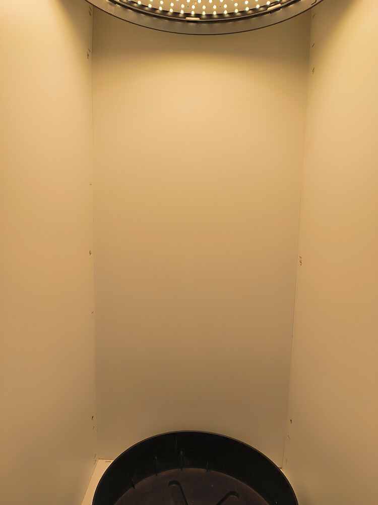 Ein leerer Grow-Raum mit einer LED-Ringlampe oben und einem schwarzen Untersetzer am Boden.