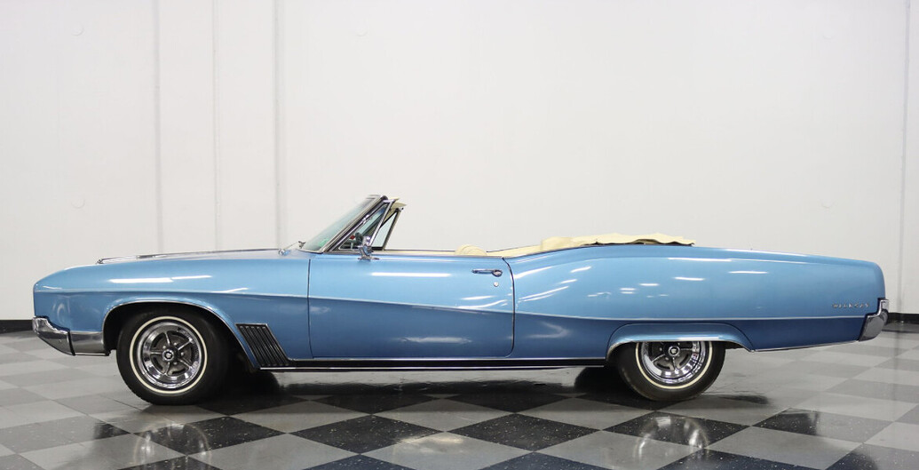 Ein blaues Oldtimer-Cabriolet steht auf einem karierten Boden vor einer weißen Wand.