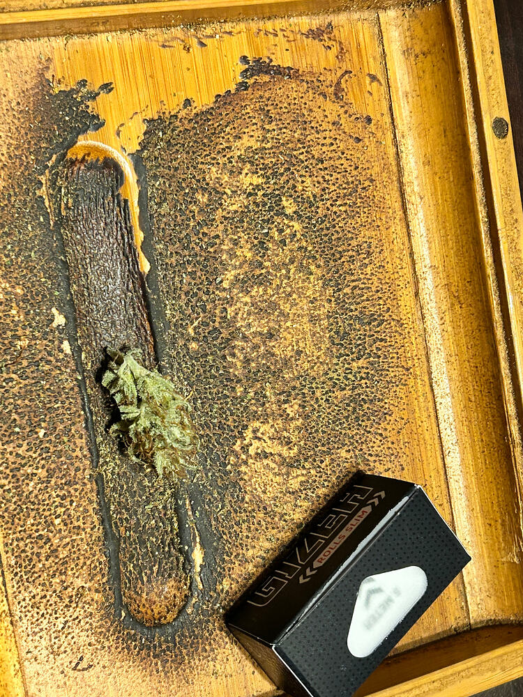 Ein einzelner, getrockneter Cannabis-Bud liegt auf einer Holzoberfläche neben einer kleinen schwarzen Schachtel mit der Aufschrift "Gizeh Rolls Slim".