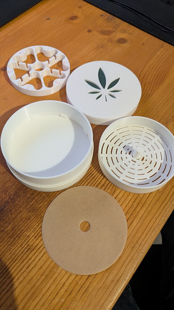 Ein zerlegter Keimungsbehälter mit einem Deckel, der ein Cannabisblatt-Symbol aufweist, sowie einem Einsatz und einem runden Filter.