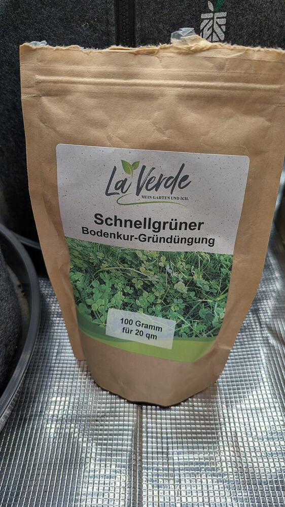 Eine braune Papiertüte mit dem Aufdruck "La Verde Schnellgrüner Bodenkur-Gründüngung" und einem Bild von grünen Pflanzen. Darunter steht "100 Gramm für 20 qm".