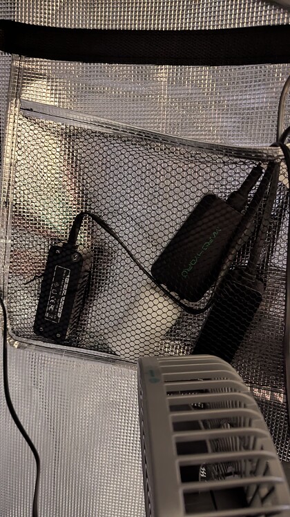 Ein schwarzes Netzfach in einer Growbox mit mehreren elektronischen Geräten, darunter ein Netzteil und zwei Controller-Einheiten.