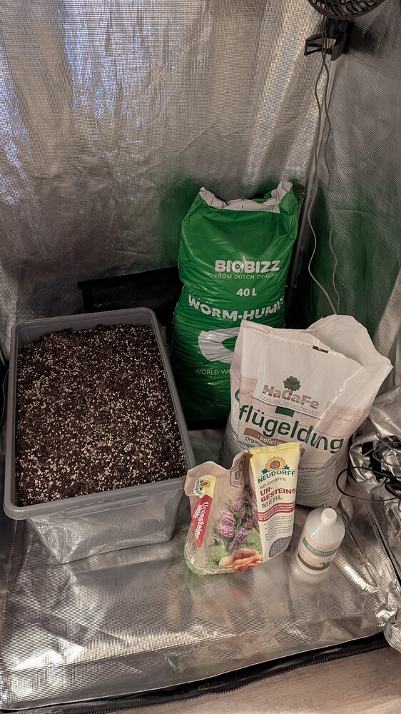 Ein Growzelt mit verschiedenen Anbauprodukten, darunter ein Behälter mit Erde, ein Sack Biobizz Worm-Humus, ein Sack Hagefe Flügeldünger und eine Flasche Flüssigdünger.